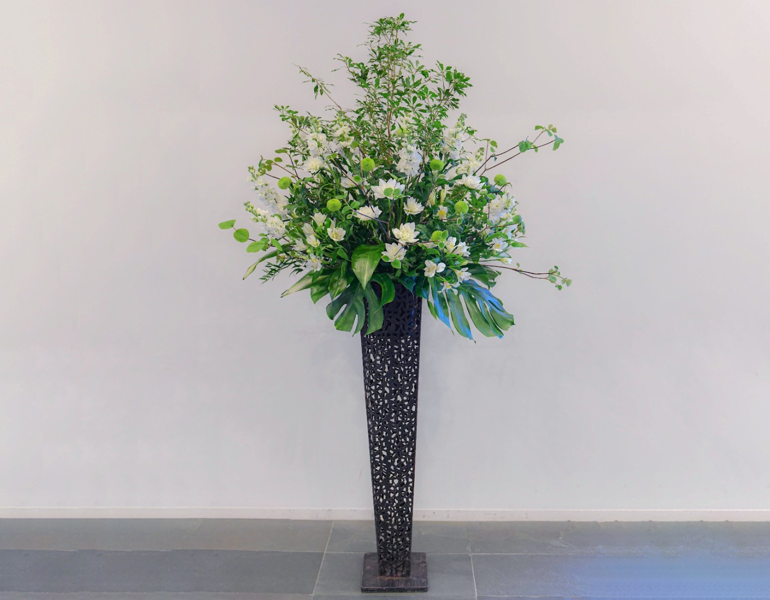 白い花と枝葉を高さのある黒い花器に生けた装花